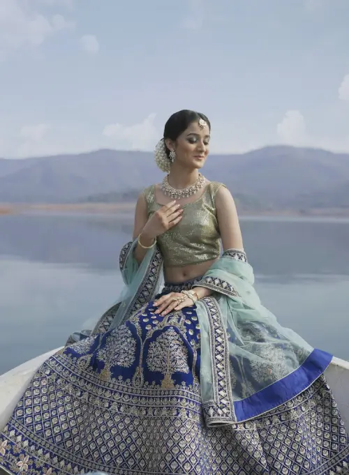 A beautiful Indian Bride wearing a beautiful blue intricate lehenga on a boat with a beautiful water background.