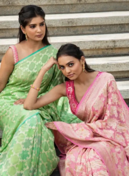 Two young Indian girls wear a green and pink sari posing aesthetically.